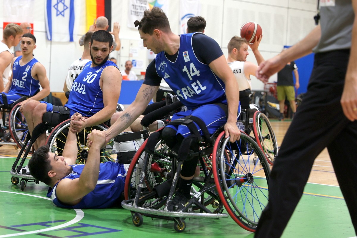 2 ספורטאים בכיסאות גלגלים עוזרים לספורטאי שלישי בכיסא, לקום מהרצפה